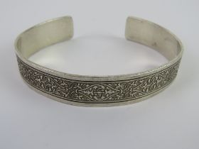 A hallmarked silver bangle having carved foliate pattern upon,