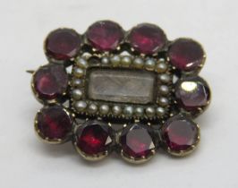 A Georgian mourning brooch having ten foil backed garnet stones around a glazed panel containing a