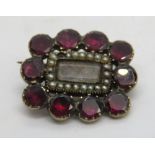 A Georgian mourning brooch having ten foil backed garnet stones around a glazed panel containing a