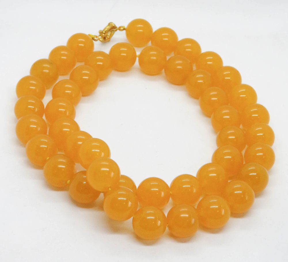A yellow Jade bead necklace strung with thread 74cm, each bead approx 20mm dia, having gilded clasp,