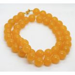 A yellow Jade bead necklace strung with thread 74cm, each bead approx 20mm dia, having gilded clasp,