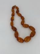 A ROW OF CYLINDRICAL GRADUATED AMBER BEADS. THE NECKLACE LENGTH 67cms. THE FITTINGS AND CAPS