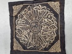 A SILVER THREAD EMBROIDERED BLACK SILK ISLAMIC PANEL WITH SCRIPT ENCLOSED BY SCROLL WORK