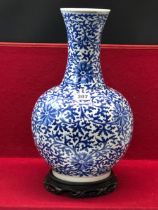 A CHINESE BLUE AND BOTTLE VASE WITH A WOOD STAND, THE PORCELAIN PAINTED OVERALL WITH SCROLLING