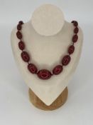 A GRADUATED ROW OF CHERRY AMBER OVAL BEADS, KNOTTED IN BETWEEN. DIAMETER SMALLEST TO LARGEST 7.5mm -