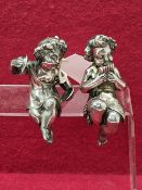 TWO VICTORIAN SILVER ELECTROPLATED PUTTO FURNITURE MOUNTS, THE SEATED FIGURES PLAYING CYMBALS AND
