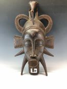 A SENUFO WOODEN MASK, THE LOOPS OF HAIR SURMOUNTED BY A BIRD PECKING THE FOREHEAD, THE SCARIFIED JAW