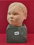 A TERRACOTTA SCULPTED HEAD OF A CHILD ON A STONE BASE. THE NECK INSCRIBED LEM OCT 63. H 31cms.