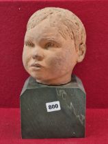 A TERRACOTTA SCULPTED HEAD OF A CHILD ON A STONE BASE. THE NECK INSCRIBED LEM OCT 63. H 31cms.