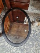 A BEVELLED GLASS OVAL MIRROR IN AN EBONISED FRAME