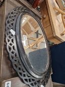 A BEVELLED GLASS OVAL MIRROR IN A BLACK PAINTED FRET WORK FRAME