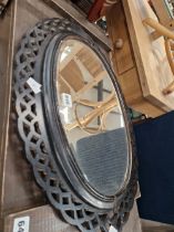 A BEVELLED GLASS OVAL MIRROR IN A BLACK PAINTED FRET WORK FRAME