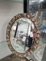 AN OVAL BEVELLED GLASS MIRROR IN A FLORAL EASEL BACKED FRAME