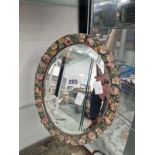 AN OVAL BEVELLED GLASS MIRROR IN A FLORAL EASEL BACKED FRAME