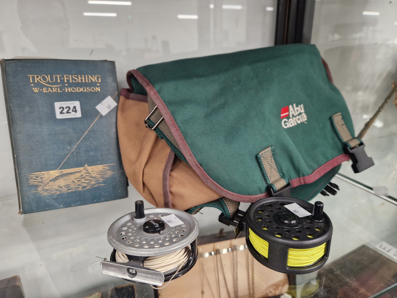 A FISHING BAG CONTAINING ACCESSORIES, TWO FLY FISHING REELS AND A BOOK: TROUT FISHING BY EARL