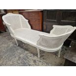 A WHITE PAINTED CANED CHAISE LONGUE, THE ROUNDED ENDS CRESTED BY CARVED FLOWERS, THE FLUTED