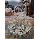 AN EIGHT LIGHT CHANDELIER, THE CREAM PAINTED FOLIATE WIRE WORK HUNG WITH PEAR SHAPED GLASS DROPS.