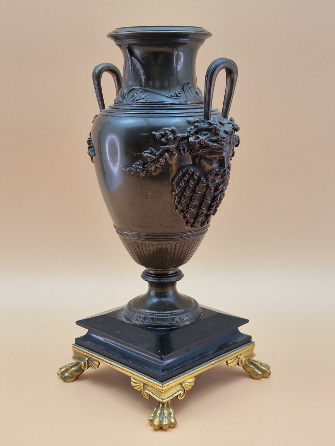 A BRONZE BALUSTER VASE, THE TWO HANDLES WITH BEARDED MASK TERMINALS, THE FOOT RESTING ON BLACK