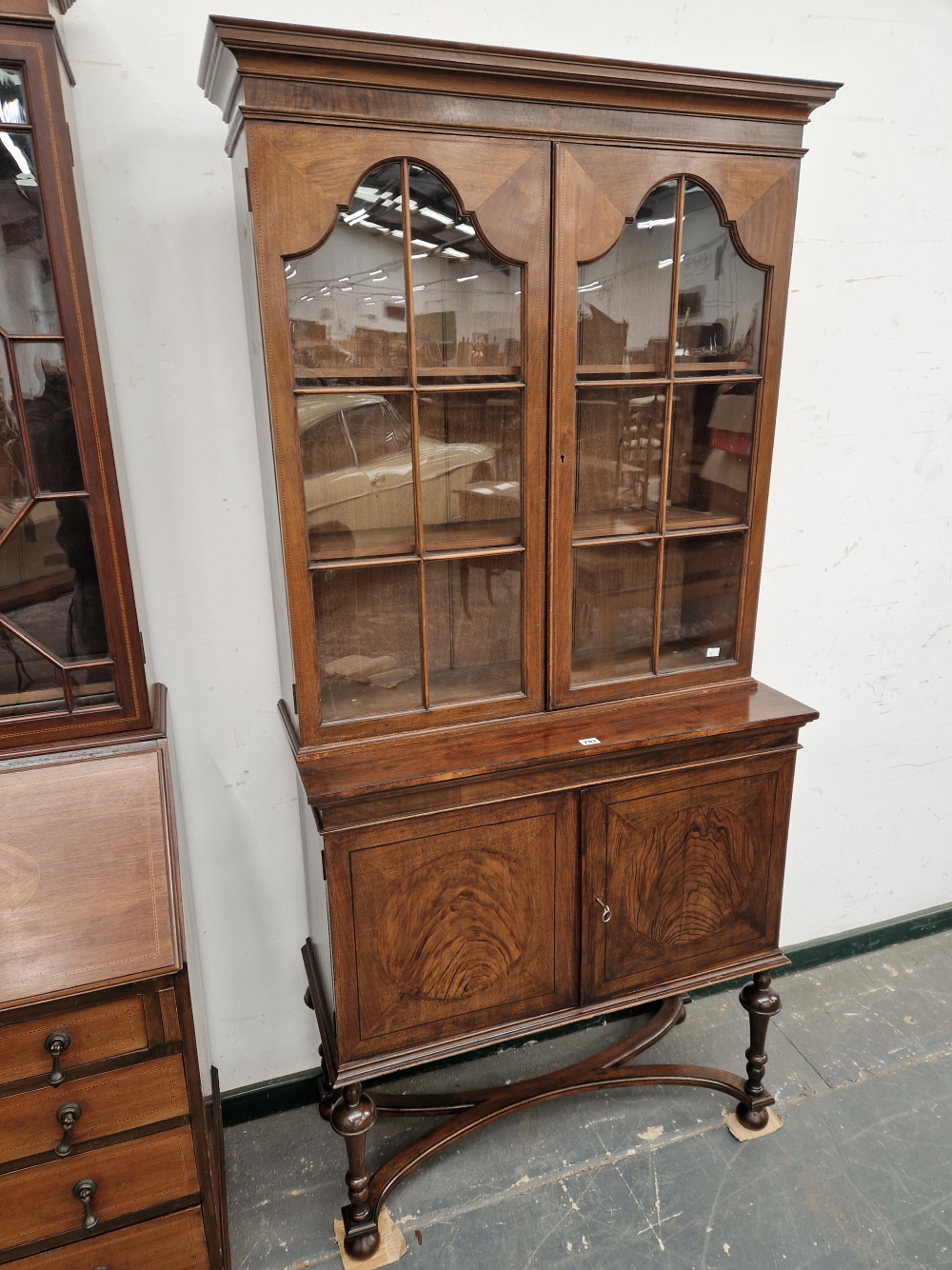 A 1920's WALNUT GLAZED CABINET ON A TWO DOOR BASE WITH BARBERS POLE LINE INLAY, THE TURNED
