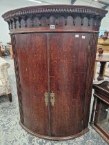 A LARGE GEORGE III OAK TWO DOOR BOW FRONT CORNER CABINET.