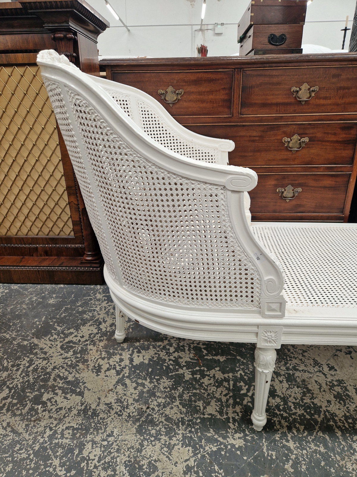 A WHITE PAINTED CANED CHAISE LONGUE, THE ROUNDED ENDS CRESTED BY CARVED FLOWERS, THE FLUTED - Image 5 of 5