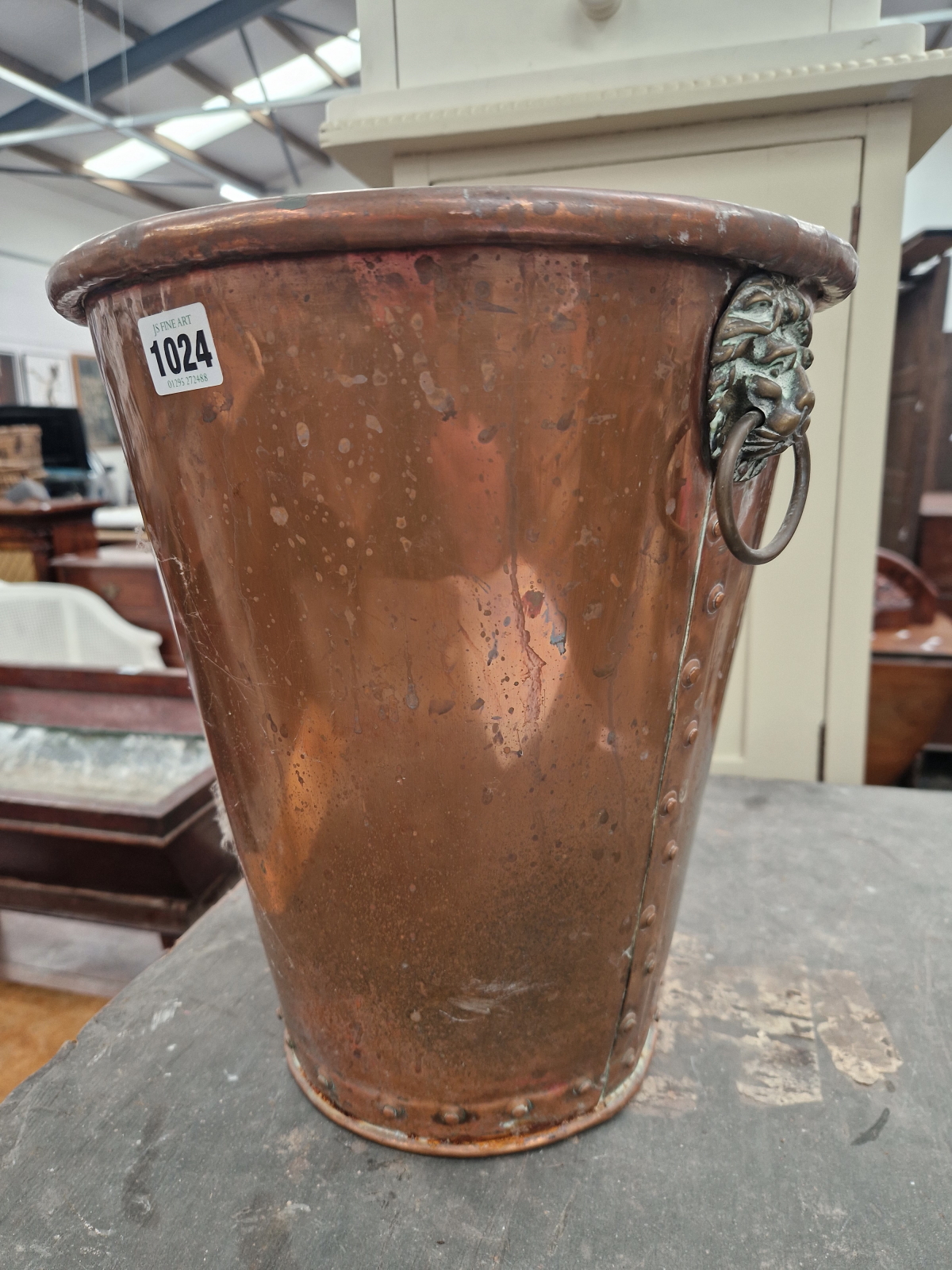 A COP[PER TAPERING CYLINDRICAL FIRE BUCKET WITH BRASS LION MASK AND RING HANDLES