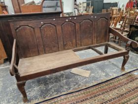 AN 18th C. OAK SETTLE WITH A FIVE PANEL BACK FLANKED BY ARMS ABOVE CABRIOLE FRONT LEGS ON PAD FEET