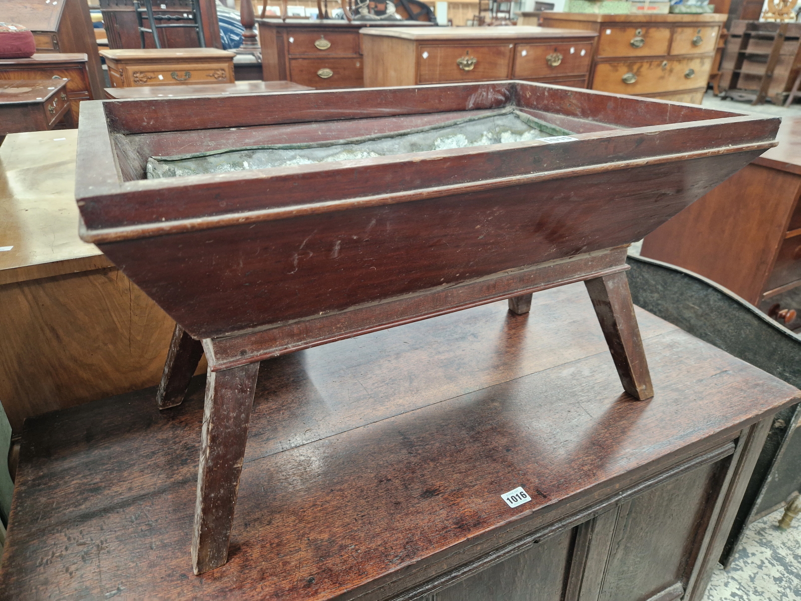 A DEEP RED PAINTED PLANTER TROUGH WITH A METAL LINER AND ON A STAND WITH FOUR SQUARE SECTIONED
