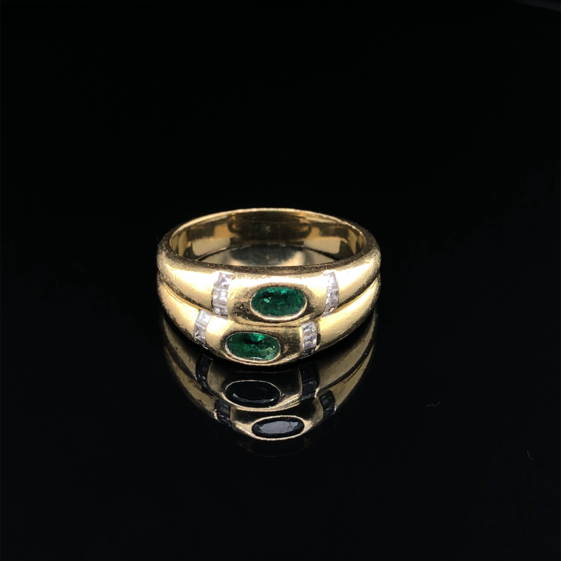 AN EMERALD AND DIAMOND RING. THE TWO OVAL CUT EMERALDS FLANKED WITH A CHANNEL SET OF PRINCESS CUT - Image 2 of 3