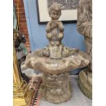 A WEATHERED COMPOSITE STONE FOUNTAIN, THE SHELL BOWL BACKED BY A CHILD SATYR PLAYING PAN PIPES.