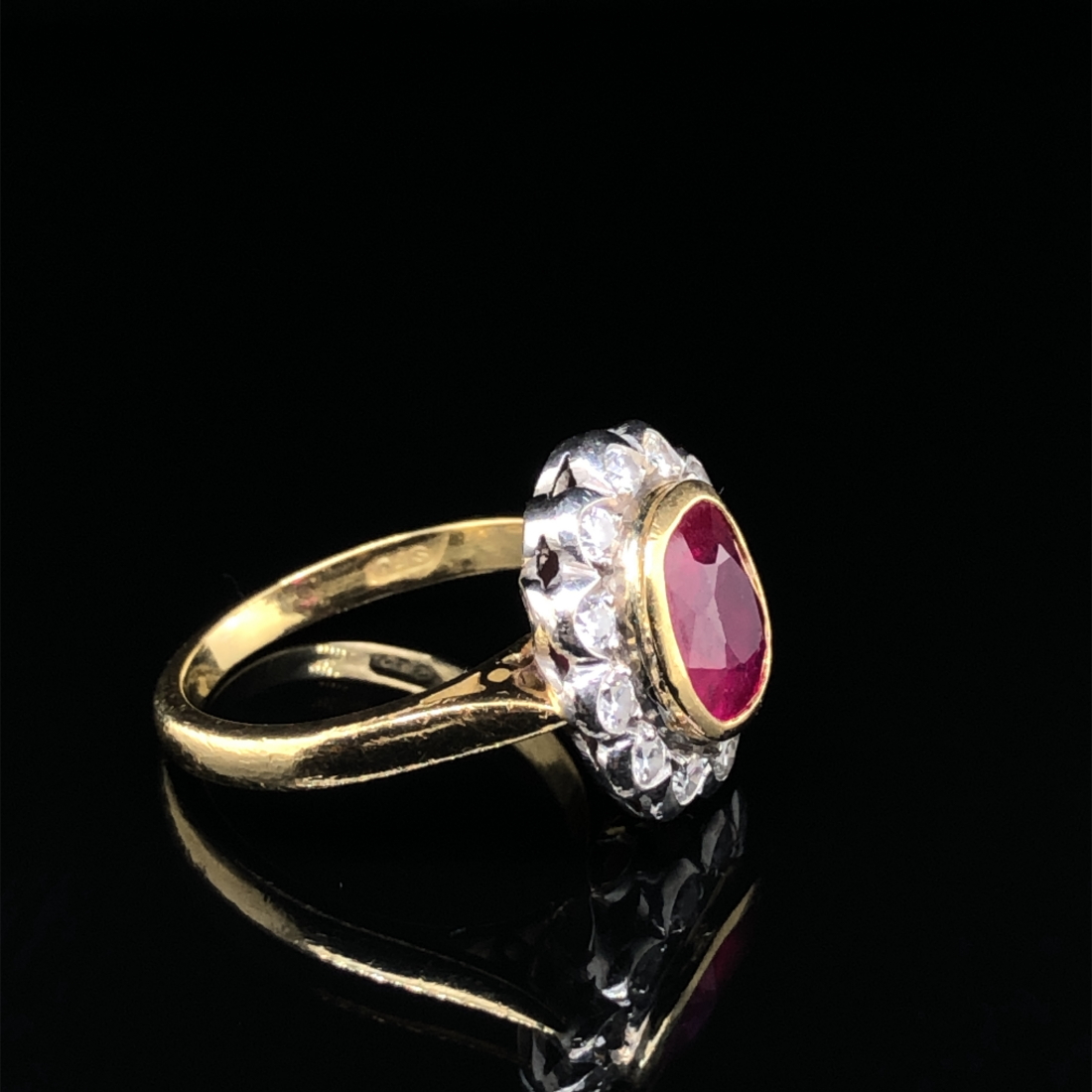 AN 18ct HALLMARKED GOLD RUBY AND DIAMOND OVAL SHAPED CLUSTER RING. THE SINGLE MEDIUM TO DARK