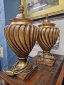 A PAIR OF GILT PLASTER TABLE LAMPS, THE WRYTHEN RIBBED CUP SHAPED BODIES SUPPORTED ON SOCLES AND