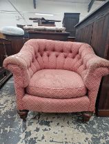 A TUB ARMCHAIR WITH A ROUNDED BUTTON UPHOLSTERED BACK, THE TURNED MAHOGANY FRONT LEGS ON BRASS