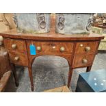 A 19TH CENTURY BOW FRONT SIDEBOARD WITH ARRANGEMENT OF DRAWERS STANDING ON SQUARE TAPERED LEGS