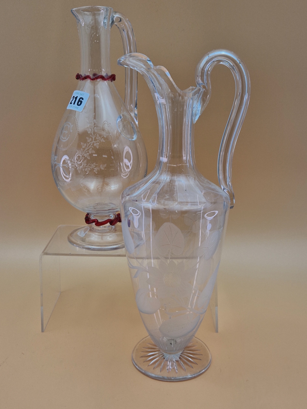 TWO LATE VICTORIAN BALUSTER GLASS EWERS, BOTHER WITH HOLLOW HANDLES, ONE ENGRAVED WITH TRAILING