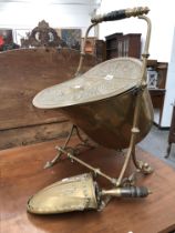 A BRASS COAL SCUTTLE AND SHOVEL, THE HELMET SHAPED BODY TILTING ON ITS STAND