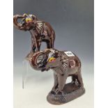 A PAIR OF TREACLE GLAZED ELEPHANT FIGURINES STANDING ON GADROON EDGED PLINTHS WITH THEIR TRUNKS