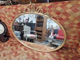 A BEVELLED GLASS OVAL MIRROR WITHIN A RIBBON TOPPED GILT FRAME