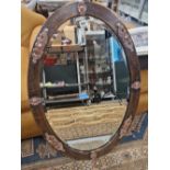 A BEVELLED GLASS OVAL MIRROR IN A HAMMERED COPPER FRAME APPLIED WITH ALTERNATING CABOCHON AND SCROLL