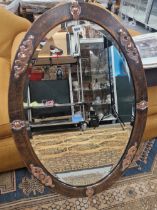 A BEVELLED GLASS OVAL MIRROR IN A HAMMERED COPPER FRAME APPLIED WITH ALTERNATING CABOCHON AND SCROLL