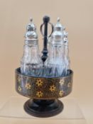 A FLORAL GILT BLACK PAPIER MACHE CRUET STAND WITH FIVE CUT GLASS BOTTLES WITH WHITE METAL MOUNTS,