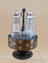 A FLORAL GILT BLACK PAPIER MACHE CRUET STAND WITH FIVE CUT GLASS BOTTLES WITH WHITE METAL MOUNTS,