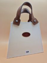 A TABLE LAMP MODELLED AS A CREAM COLOURED HANDBAG WITH BROWN LEATHER HANDLES. H 37cms.