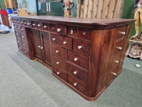 A MAHOGANY SHOP COUNTER FITTED WITH MULTIPLE DRAWERS AND CUPBOARDS EACH WITH WHITE CERAMIC KNOB