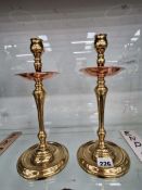 A pair of W.A.S. Benson brass candlesticks with copper drip pans