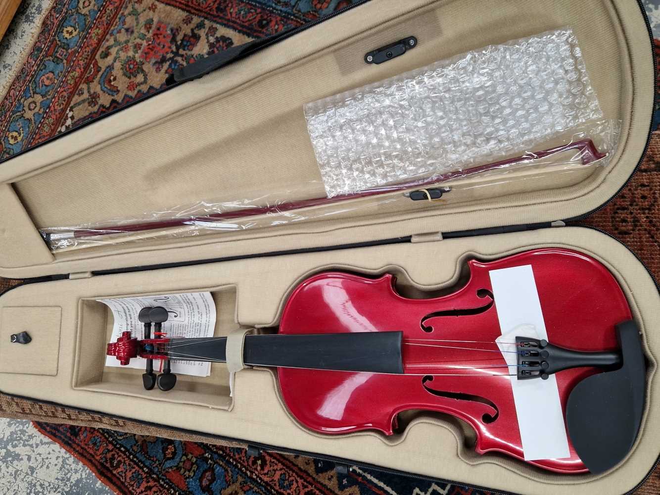 A full size violin with red lacquer body, in fitted case with bow.