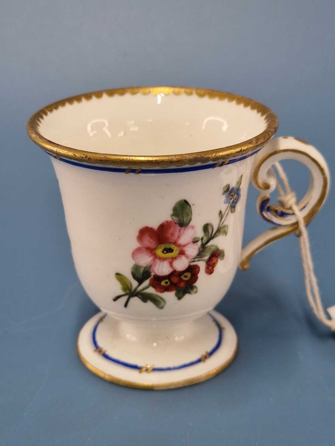 A Sevres ice cup painted with a blue line and flower sprays below a gilt dentil rim line The