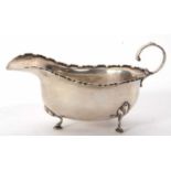 A George V silver sauce boat of typical form having castellated edge, capped scroll handle and