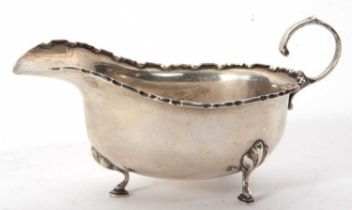 A George V silver sauce boat of typical form having castellated edge, capped scroll handle and