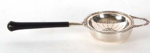 A hallmarked silver tea strainer and drip bowl with circular pierced design, applied scroll edge and